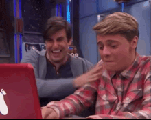 two men are laughing and looking at a laptop