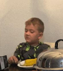 a little boy is sitting at a table eating corn on the cob