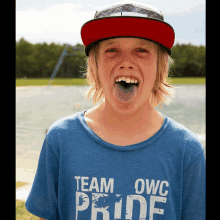 a boy wearing a hat and a blue shirt that says team owc pride sticking his tongue out