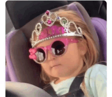 a little girl is sitting in a car seat wearing a tiara and sunglasses .