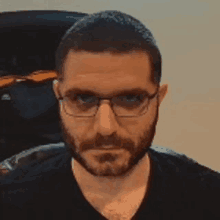 a man with a beard is wearing glasses and a black shirt .