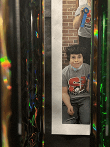 a boy wearing a gray shirt with the letter s on it is sitting in front of a mirror