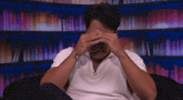 a man in a white shirt covering his eyes with his hands