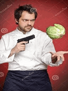 a man in a chef 's uniform is holding a gun and a cabbage .