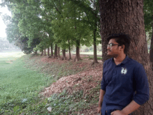 a man leaning against a tree with a shirt that says ' a ' on the front