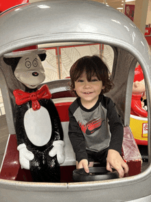 a little boy wearing a nike shirt sits in a car next to a cat in the hat statue