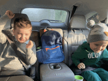 two young boys in the back seat of a car one wearing a green hoodie that says old