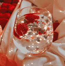 a glass filled with strawberries and flowers on a cloth