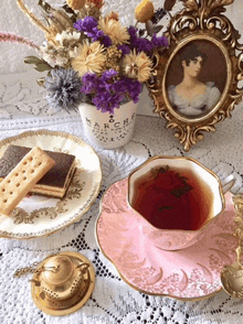 a cup of tea sits on a pink saucer next to a plate of cookies