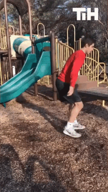 a boy in a red shirt is doing squats in front of a slide at a playground with the letters th on the bottom