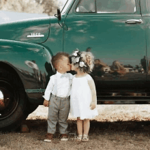 a little boy and a little girl are kissing in front of a green truck .