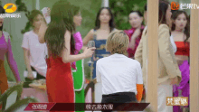 a woman in a red dress stands in front of a group of women with chinese writing on the bottom