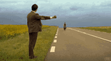 a man in a suit is standing on the side of a road while a man on a motorcycle passes by