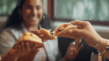 a woman is sitting at a table eating a sandwich while another woman holds a sandwich in her hand .