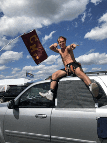 a shirtless man is sitting on the roof of a car with a cmp flag behind him