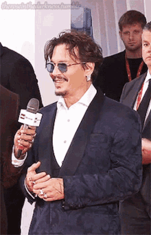 a man wearing sunglasses and a suit is holding a microphone