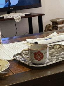 a cup with a red flower on it sits on a tray on a table in front of an lg tv