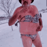 a shirtless man wearing a bikini and a cowboy hat is standing in the snow .