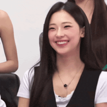 a woman wearing a white shirt and black vest smiles