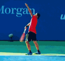 a man in a red shirt is holding a tennis racquet on a tennis court in front of a sign that says morgan