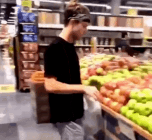 a man in a black shirt is standing in front of a display of apples in a grocery store .