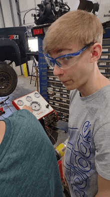 a young man wearing safety glasses and an adidas shirt stands in front of a machine