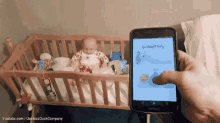 a person is holding a cell phone in front of a baby in a crib and it says goodnight baby on the screen