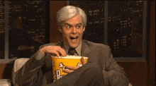 a man in a suit is eating a bucket of popcorn .