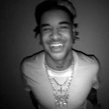 a black and white photo of a man wearing a hat and a necklace and smiling .