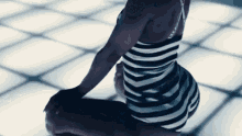 a woman in a black and white striped dress is kneeling on a dance floor .