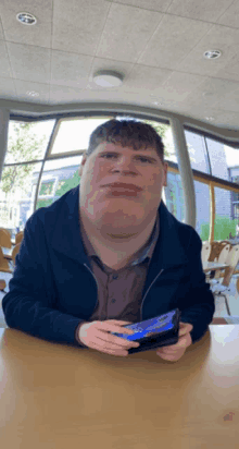 a man sitting at a table holding a cell phone and making a funny face