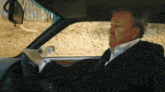 a man in a suit is driving a car and looking at his watch