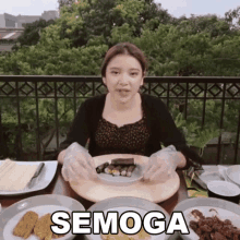 a woman is sitting at a table with plates of food and a plate of food with the word semoga on it .