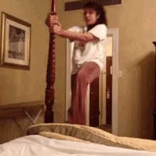 a woman in a white shirt is jumping off a bed post