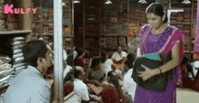 a woman in a purple sari is standing in front of a crowd of people in a clothing store .