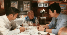 three men are sitting at a table with a sign that says beaujolais in the background