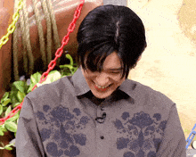 a man wearing a grey shirt with a floral design on it smiles