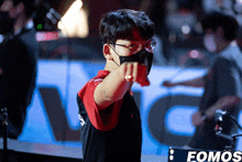 a man wearing glasses and a mask pointing at the camera in front of a sign that says fomos