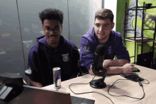 a can of red bull sits on a desk next to two men