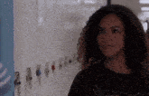 a girl with curly hair is standing in front of a row of lockers in a school hallway .