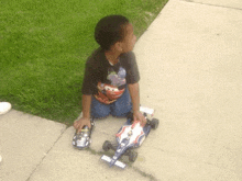 a boy wearing a lightning mcqueen shirt sits on the sidewalk playing with a toy car