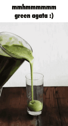 a green smoothie is being poured into a glass on a wooden table