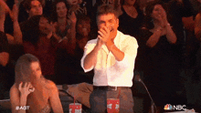 a man in a white shirt is clapping in front of a crowd with a coca cola cup in his hand