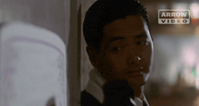 a man leaning against a wall with an arrow video logo in the background