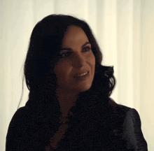 a woman with dark hair is smiling in front of a white wall