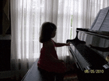 a little girl in a red dress playing a piano