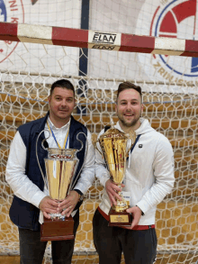 two men holding trophies in front of a elan banner