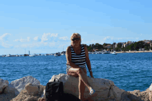 a woman sits on a rock near the water