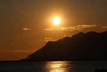 the sun is setting over a body of water with a mountain in the background