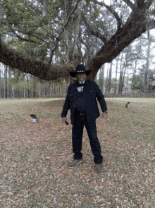 a man wearing a cowboy hat is standing in front of a tree with spanish moss